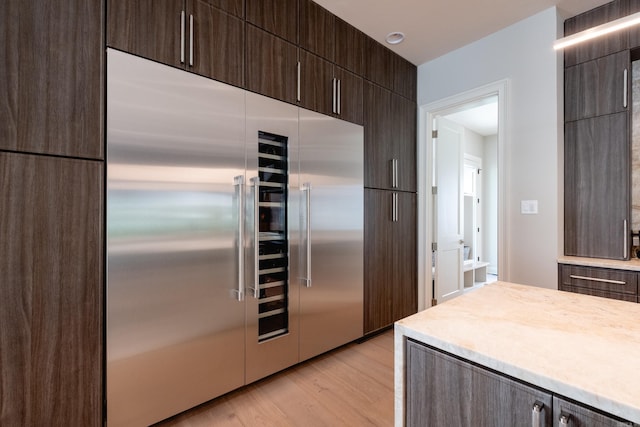 kitchen with light wood-type flooring, built in fridge, and dark brown cabinetry