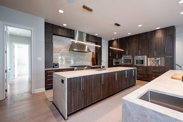 kitchen with a kitchen island with sink, appliances with stainless steel finishes, sink, range hood, and tasteful backsplash