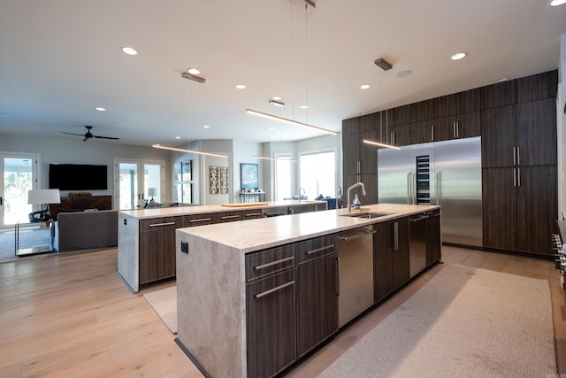 kitchen featuring stainless steel appliances, sink, ceiling fan, light hardwood / wood-style floors, and a center island with sink