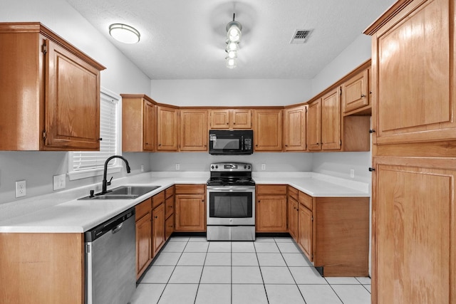 kitchen with appliances with stainless steel finishes, sink, light tile patterned floors, and a textured ceiling