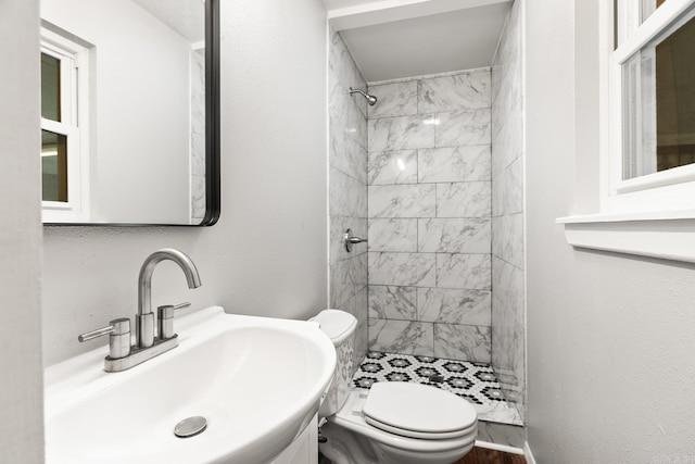 bathroom featuring toilet, a tile shower, and sink