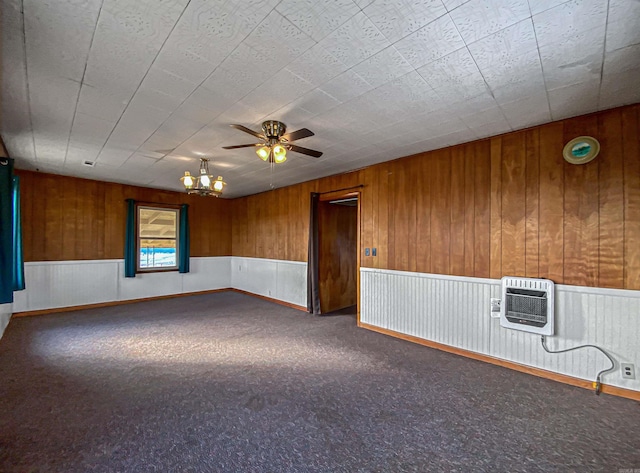 spare room with heating unit, wood walls, carpet floors, and ceiling fan with notable chandelier