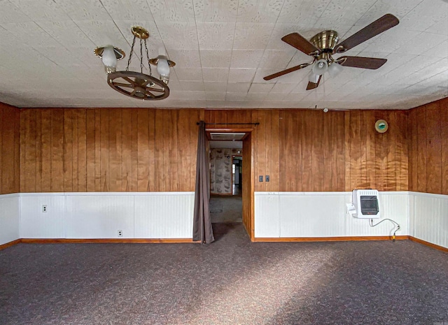 carpeted spare room with ceiling fan with notable chandelier, heating unit, and wood walls