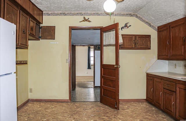 kitchen featuring vaulted ceiling, white refrigerator, and a textured ceiling