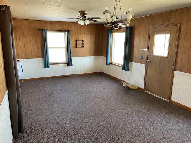 carpeted empty room featuring ceiling fan with notable chandelier, plenty of natural light, and radiator