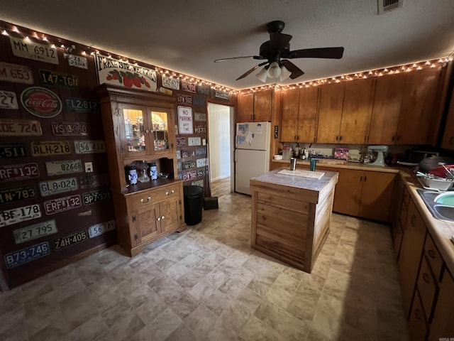 kitchen with white fridge, ceiling fan, tile counters, a center island, and sink