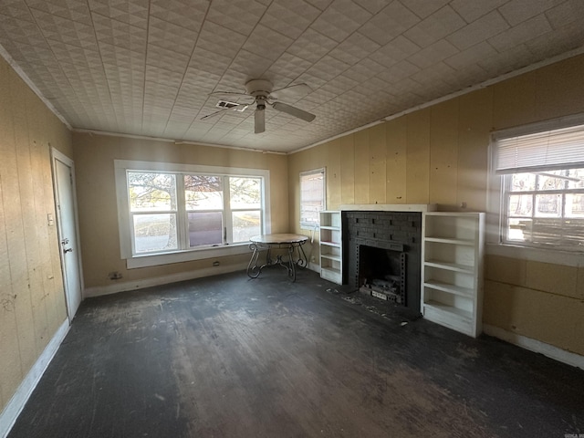 unfurnished living room featuring a brick fireplace, wood walls, ceiling fan, and crown molding