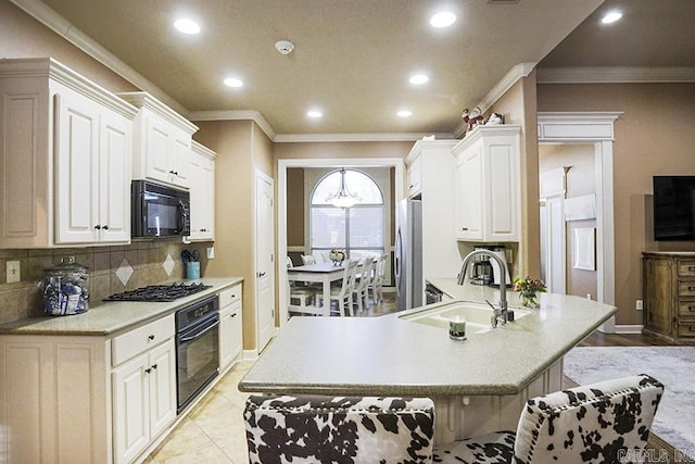 kitchen featuring black appliances, backsplash, white cabinets, a kitchen breakfast bar, and sink