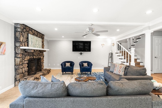 tiled living room with ceiling fan, a stone fireplace, and crown molding