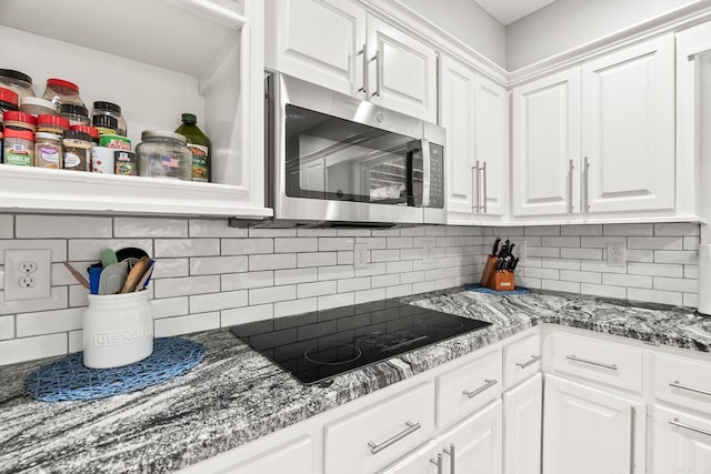 kitchen with white cabinets, black electric stovetop, dark stone countertops, and decorative backsplash