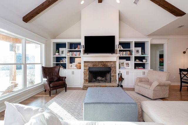 living room featuring lofted ceiling with beams, a healthy amount of sunlight, light hardwood / wood-style flooring, and a stone fireplace