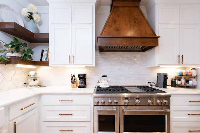 kitchen with white cabinets, range with two ovens, custom exhaust hood, and decorative backsplash