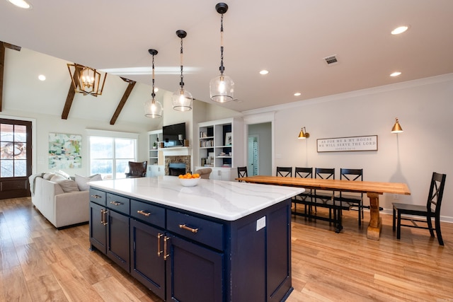 kitchen with a stone fireplace, blue cabinetry, a center island, pendant lighting, and light stone counters