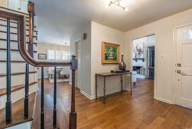 entryway with dark wood-type flooring, an inviting chandelier, and a fireplace