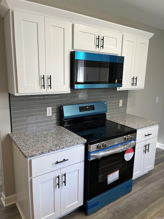 kitchen with electric range, light wood-type flooring, light stone countertops, decorative backsplash, and white cabinets