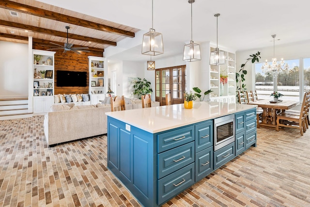 kitchen with blue cabinets, stainless steel microwave, beam ceiling, and hanging light fixtures