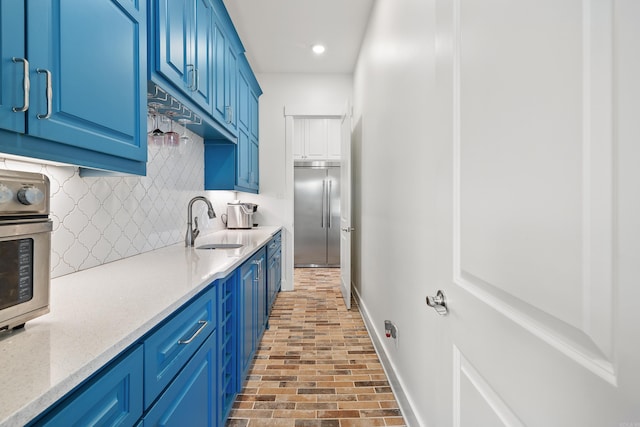 kitchen featuring blue cabinetry, stainless steel built in refrigerator, light stone countertops, decorative backsplash, and sink