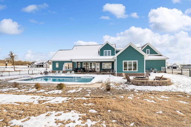 snow covered rear of property with an outdoor fire pit and a fenced in pool