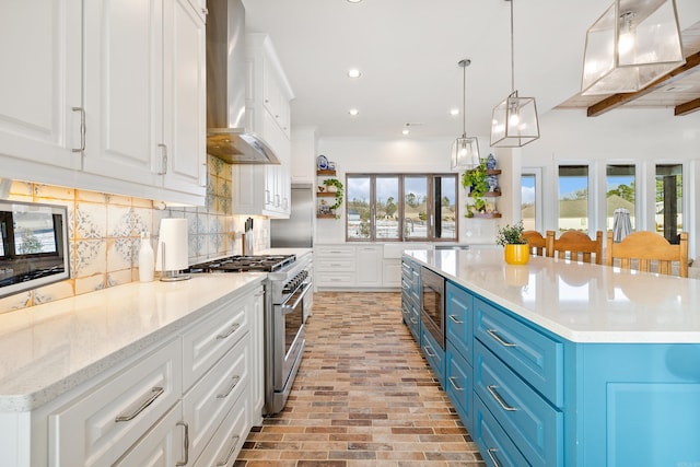 kitchen featuring wall chimney exhaust hood, decorative backsplash, white cabinetry, blue cabinets, and appliances with stainless steel finishes