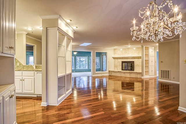 unfurnished living room featuring a notable chandelier, hardwood / wood-style floors, built in shelves, crown molding, and a fireplace