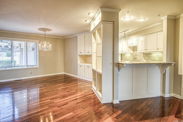 kitchen with kitchen peninsula, light stone countertops, hanging light fixtures, decorative backsplash, and white cabinetry