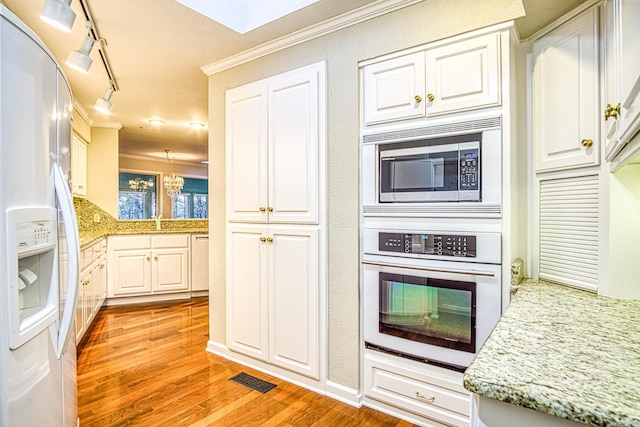 kitchen featuring light stone counters, an inviting chandelier, crown molding, white cabinetry, and appliances with stainless steel finishes