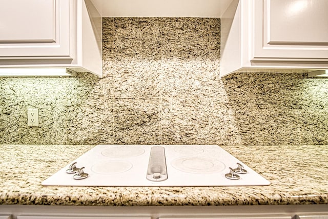 interior details with white cabinetry, white electric cooktop, backsplash, and light stone countertops