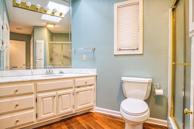 bathroom featuring toilet, wood-type flooring, a skylight, vanity, and a shower with door