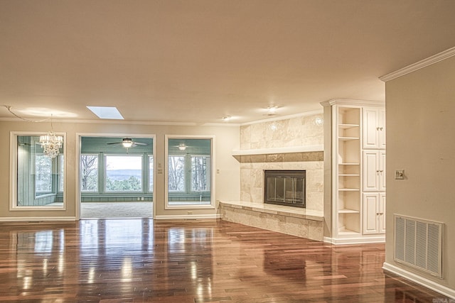 unfurnished living room featuring a chandelier, dark hardwood / wood-style floors, built in shelves, a skylight, and ornamental molding