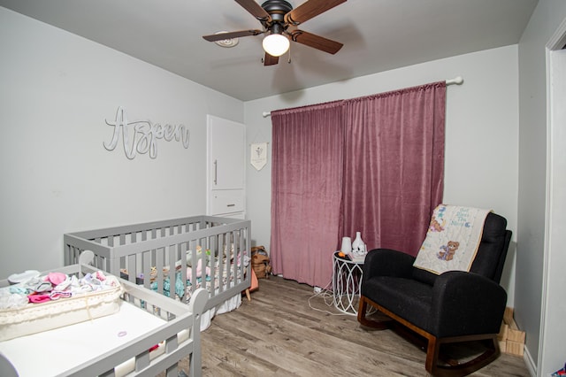 bedroom featuring light wood-type flooring, ceiling fan, and a crib