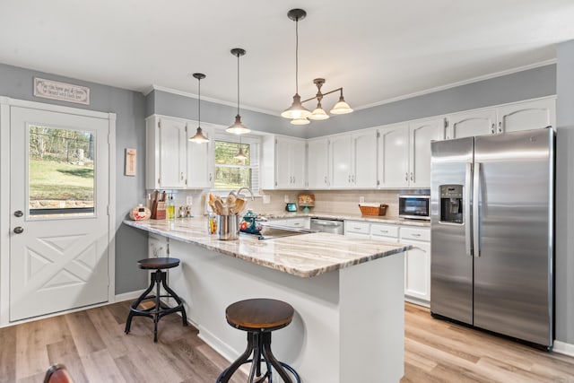 kitchen with kitchen peninsula, decorative light fixtures, stainless steel appliances, white cabinetry, and a kitchen breakfast bar