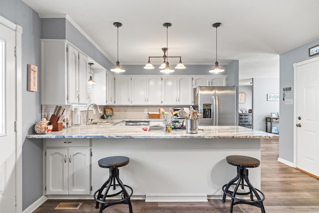 kitchen with sink, light stone counters, kitchen peninsula, stainless steel fridge with ice dispenser, and pendant lighting