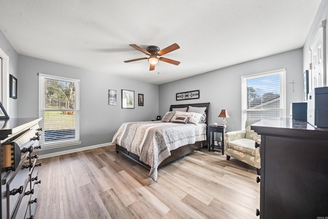 bedroom with a textured ceiling, ceiling fan, light hardwood / wood-style floors, and multiple windows