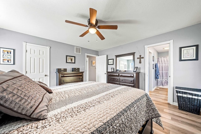 bedroom featuring ceiling fan, light hardwood / wood-style flooring, ensuite bath, and a textured ceiling