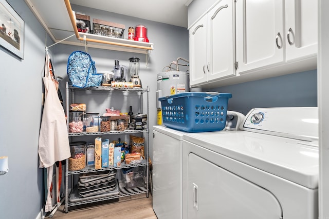 washroom featuring water heater, cabinets, washing machine and clothes dryer, and light hardwood / wood-style floors