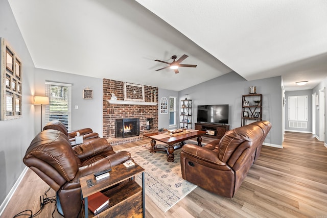 living room with ceiling fan, light hardwood / wood-style floors, vaulted ceiling, and a fireplace