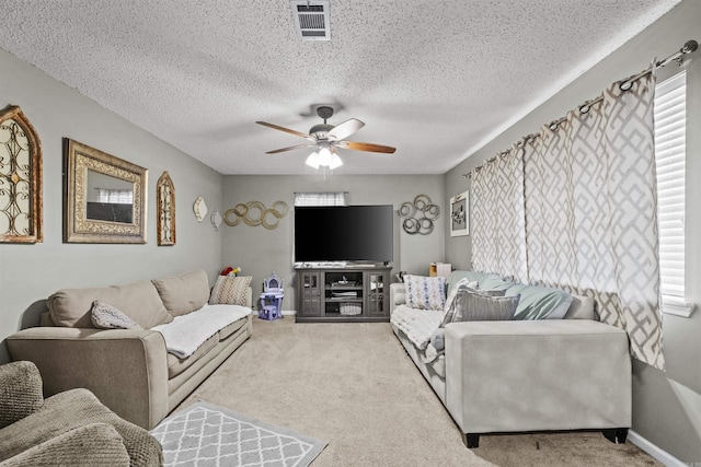 living room with a textured ceiling, ceiling fan, a wealth of natural light, and light colored carpet