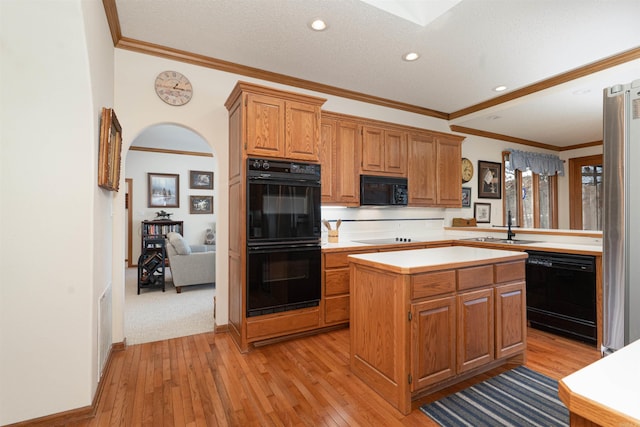 kitchen with crown molding, light wood-type flooring, black appliances, and a center island