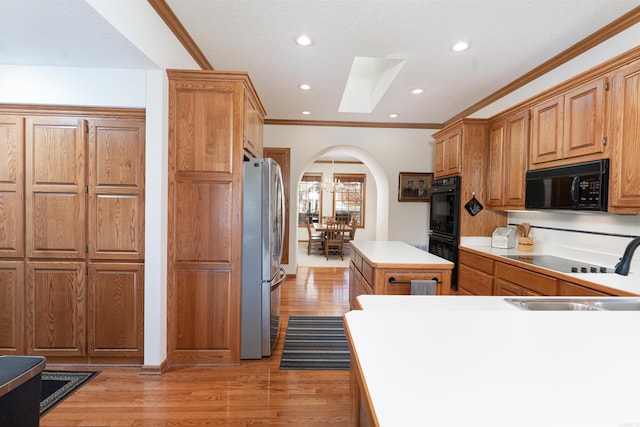 kitchen featuring black appliances, light hardwood / wood-style floors, crown molding, a kitchen island, and sink