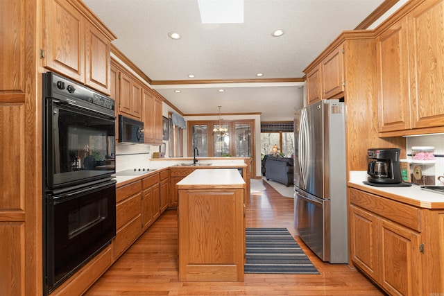 kitchen with black appliances, a center island, ornamental molding, sink, and light hardwood / wood-style flooring