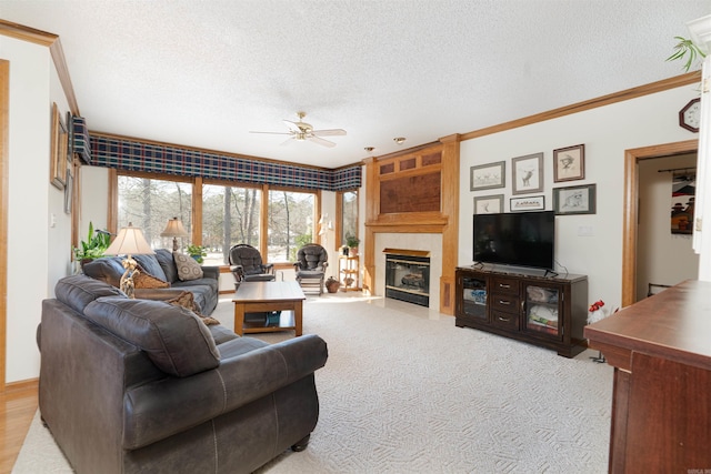 living room with a textured ceiling, a tile fireplace, ornamental molding, ceiling fan, and light carpet