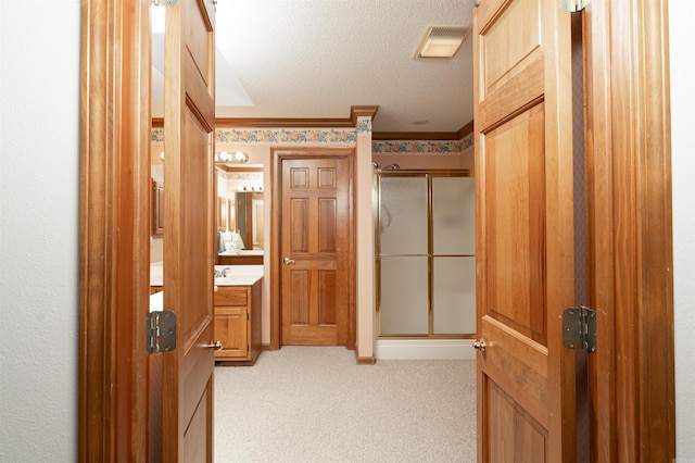 hallway featuring a textured ceiling, ornamental molding, and light carpet