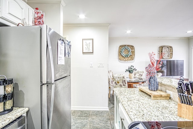 kitchen featuring light stone countertops, white cabinets, crown molding, and stainless steel fridge