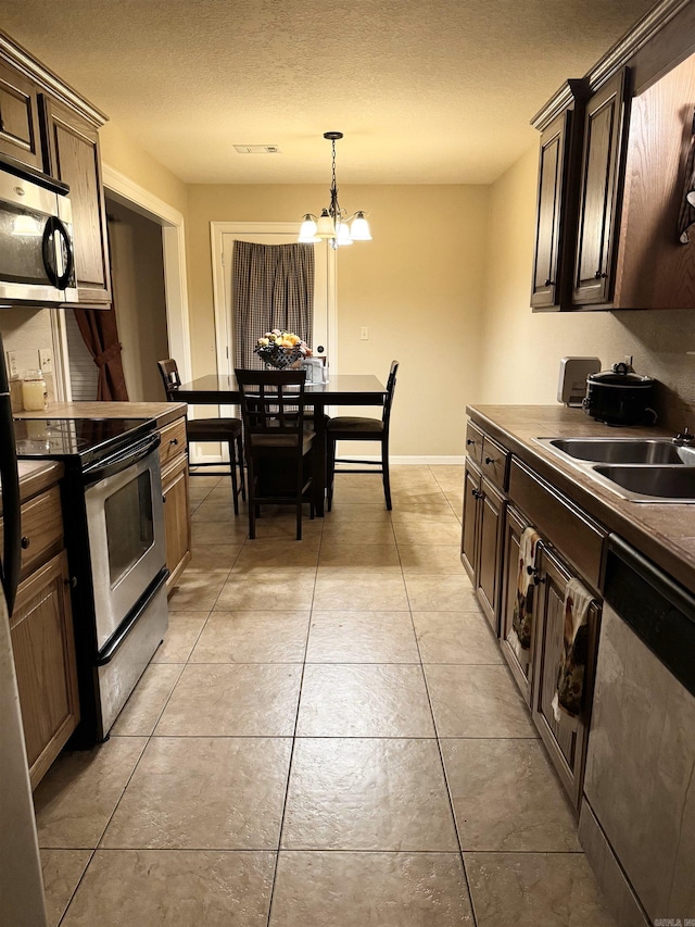 kitchen with appliances with stainless steel finishes, light tile patterned floors, a notable chandelier, a textured ceiling, and sink