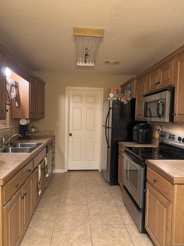 kitchen featuring a textured ceiling, appliances with stainless steel finishes, light tile patterned flooring, and sink