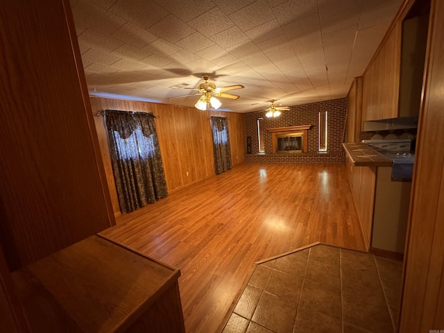 unfurnished living room featuring hardwood / wood-style floors, a fireplace, ceiling fan, and wood walls