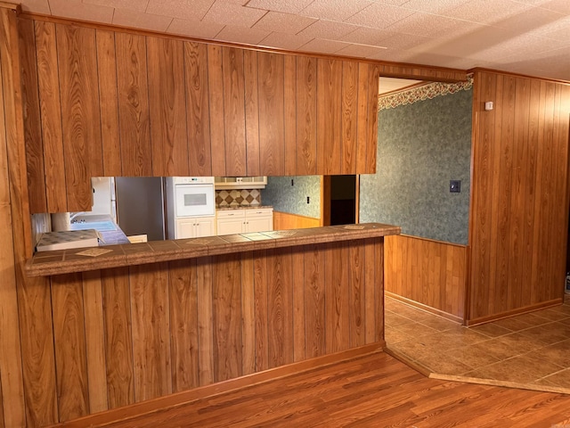 kitchen with wood-type flooring, white oven, stainless steel refrigerator, kitchen peninsula, and wooden walls