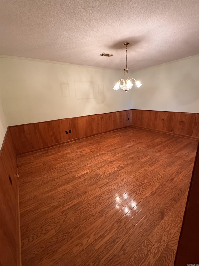 empty room with a textured ceiling, dark hardwood / wood-style flooring, and a chandelier