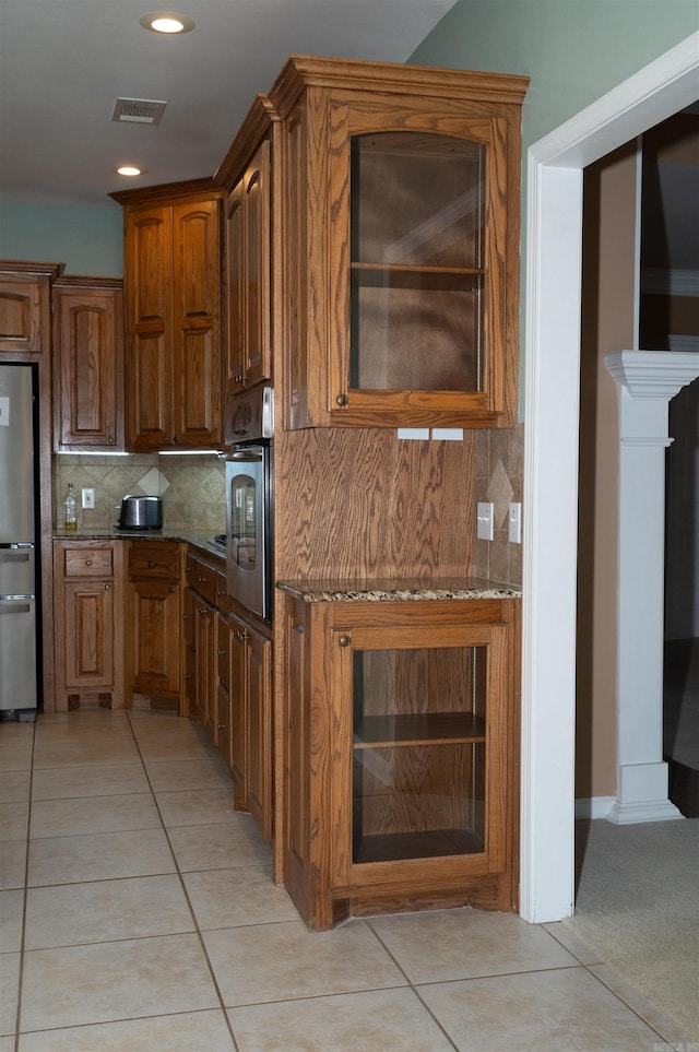 kitchen with stainless steel appliances, dark stone countertops, light tile patterned floors, and tasteful backsplash