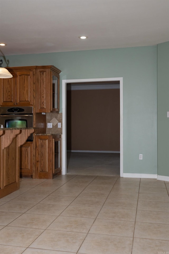 kitchen with backsplash, stainless steel oven, dark stone countertops, and light tile patterned floors